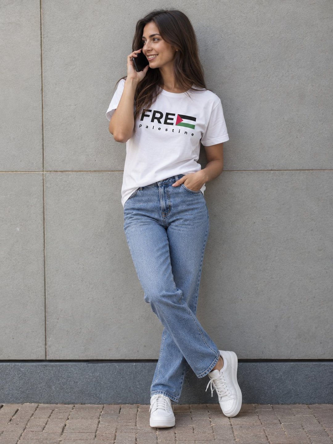 Woman in a Free Palestine t-shirt and jeans leaning against a city wall